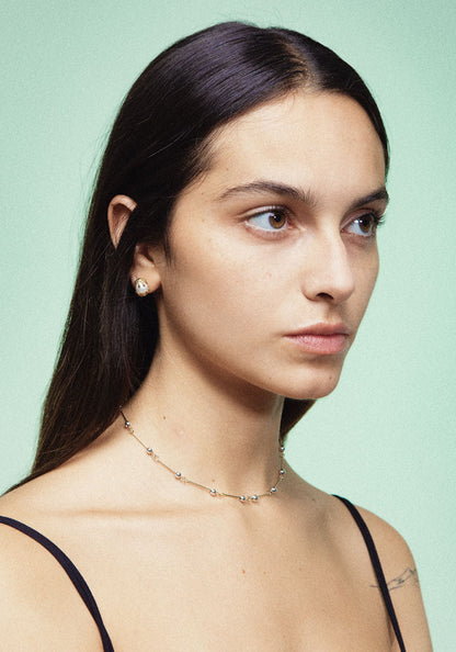 A pair of gold earrings featuring a white pearl in between, designed to resemble a chicken hatching from an egg. Handmade in Barcelona. 