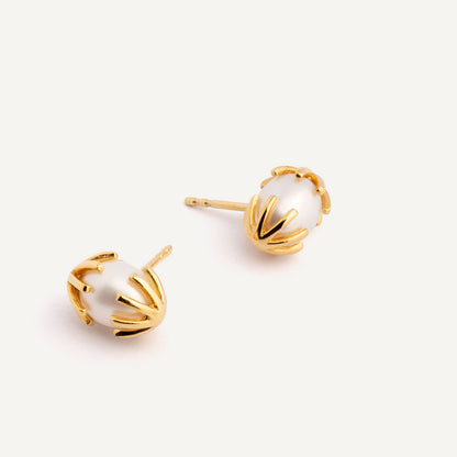 A pair of gold earrings featuring a white pearl in between, designed to resemble a chicken hatching from an egg. Handmade in Barcelona. 