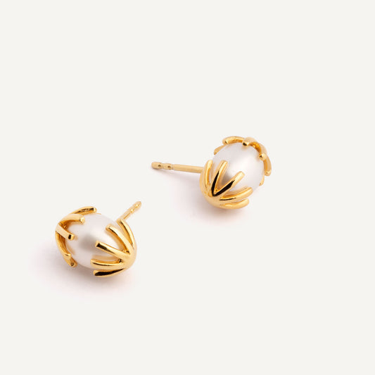 A pair of gold earrings featuring a white pearl in between, designed to resemble a chicken hatching from an egg. Handmade in Barcelona. 