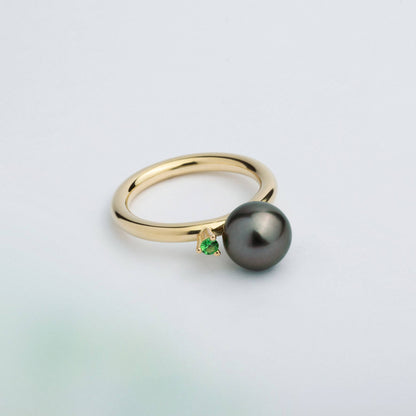 A ring with a large grey Freshwater Pearl set in a 18K gold wire, with a tall prong setting holding a bright green Tsavorite Garnet.