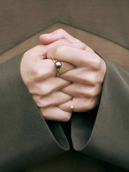 A ring with a large grey Freshwater Pearl set in a 18K gold wire, with a tall prong setting holding a bright green Tsavorite Garnet.