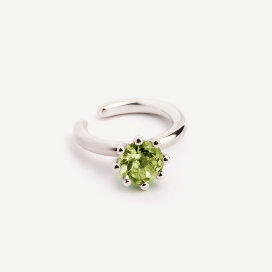 A green ear cuff ring with a peridot stone, made of silver, displayed on a white background.