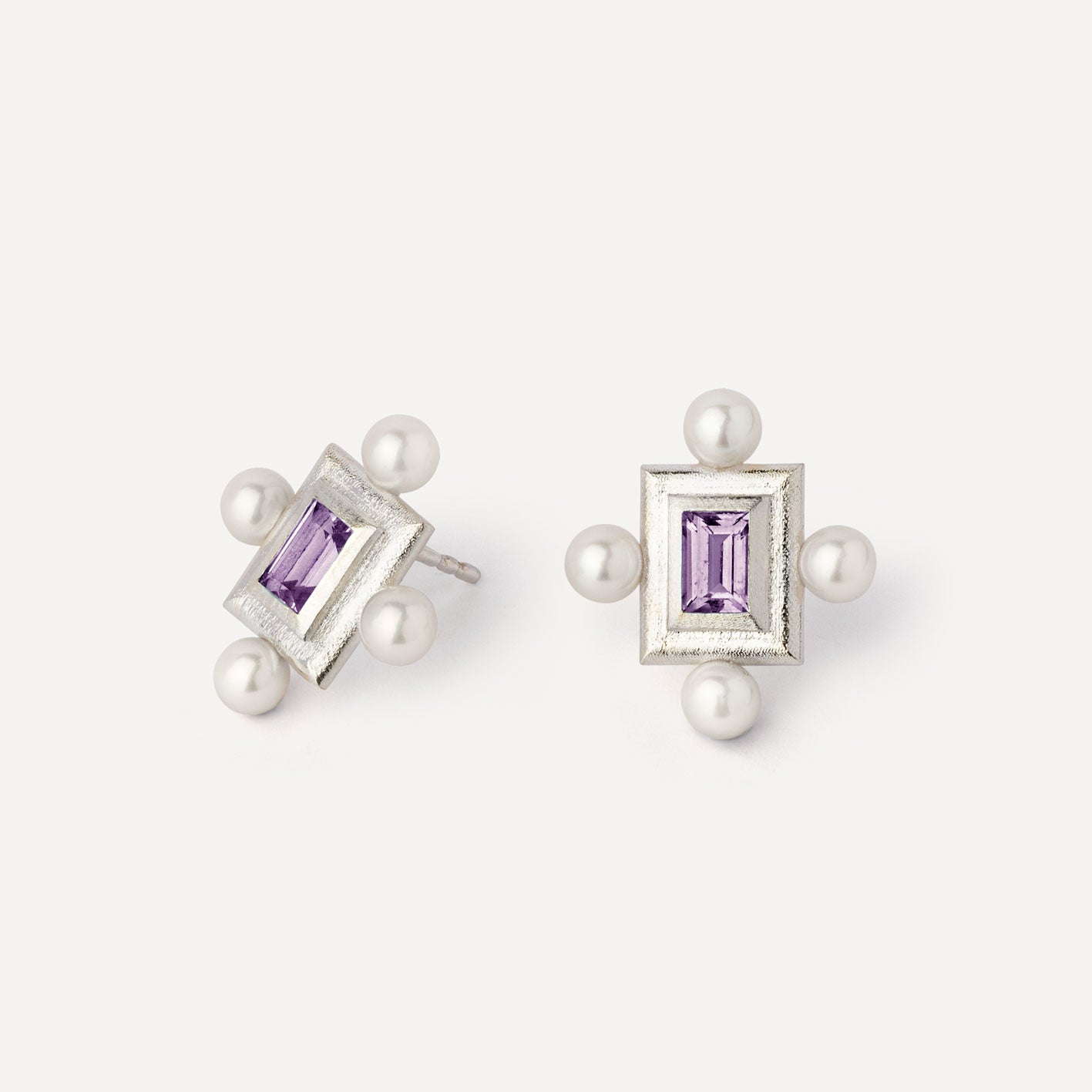 A pair of silver earrings featuring a geometric design with a central violet gemstone surrounded by pearls, set in a rectangular shape.