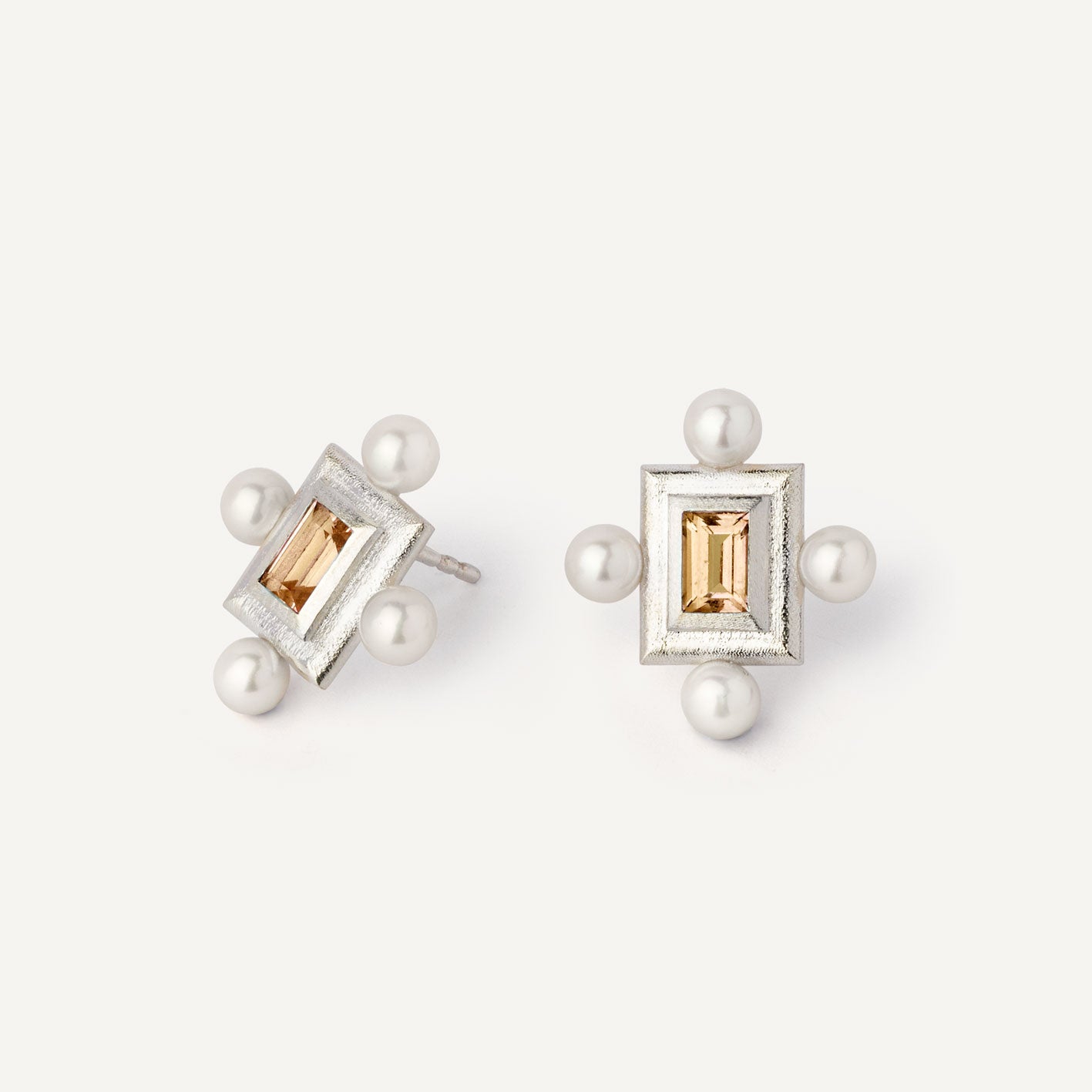 A pair of silver earrings featuring a geometric design with a central yellow gemstone surrounded by pearls, set in a rectangular shape.