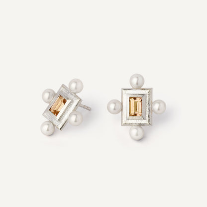 A pair of silver earrings featuring a geometric design with a central yellow gemstone surrounded by pearls, set in a rectangular shape.