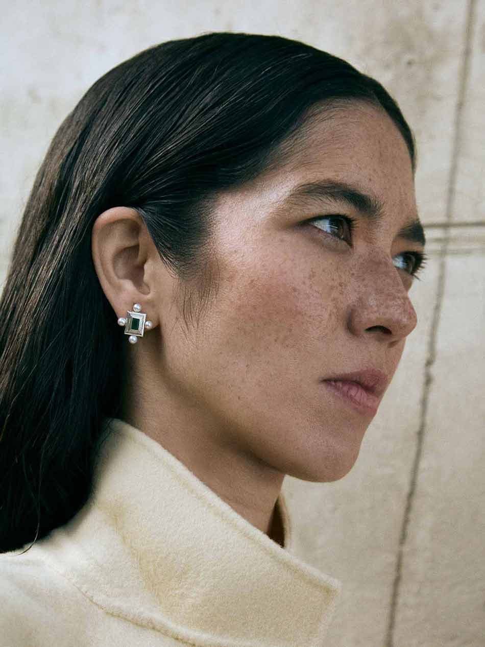 A pair of silver earrings featuring a geometric design with a central colored gemstone surrounded by pearls, set in a rectangular shape.