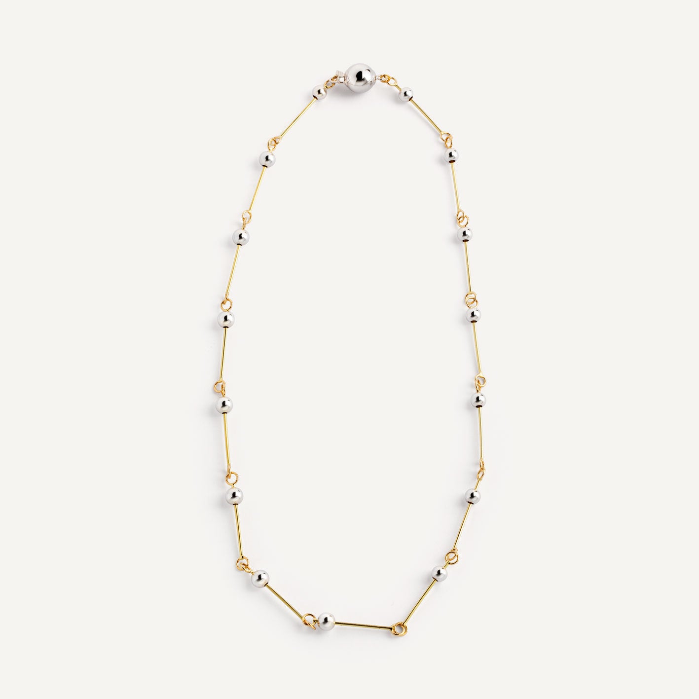A necklace with small silver spheres strung on gold wire, with a focus on the interplay of light and shadow.