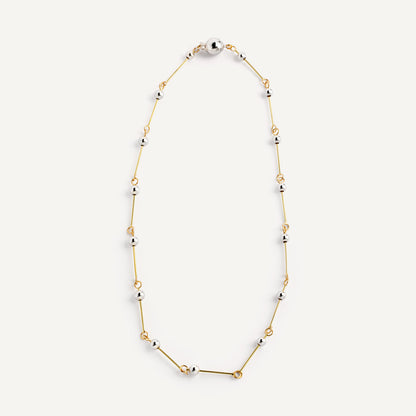 A necklace with small silver spheres strung on gold wire, with a focus on the interplay of light and shadow.
