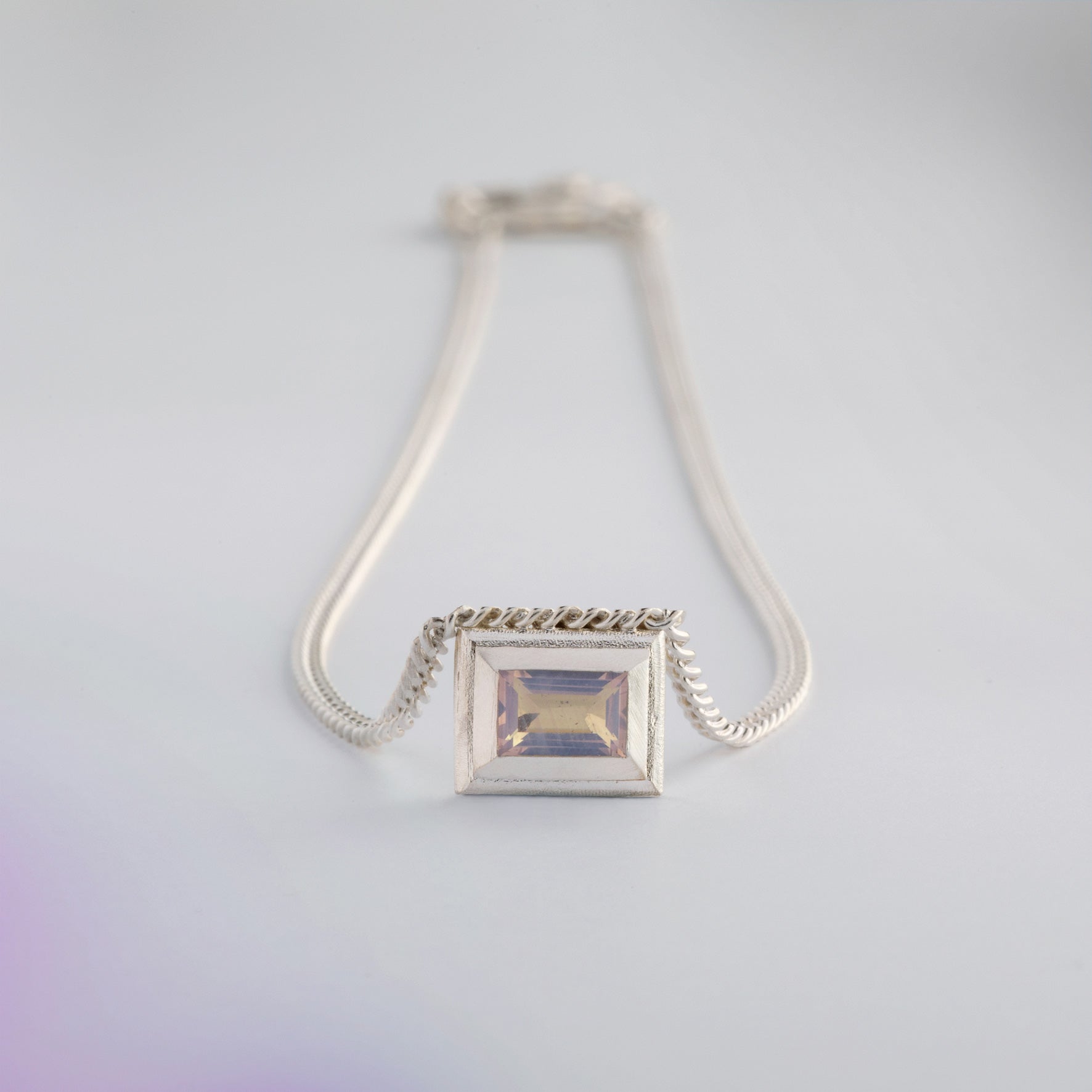 A silver necklace with a reversible pendant featuring a green Peridot gemstone on one side and violet Amethyst on the other designed for everyday wear.