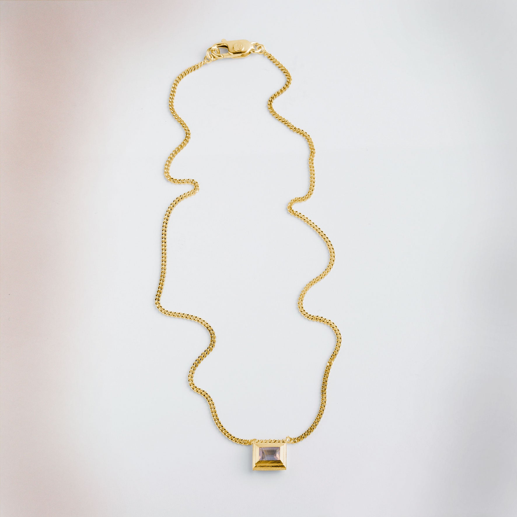 A gold plated silver necklace with a reversible pendant featuring a green Peridot gemstone on one side and violet Amethyst on the other designed for everyday wear.