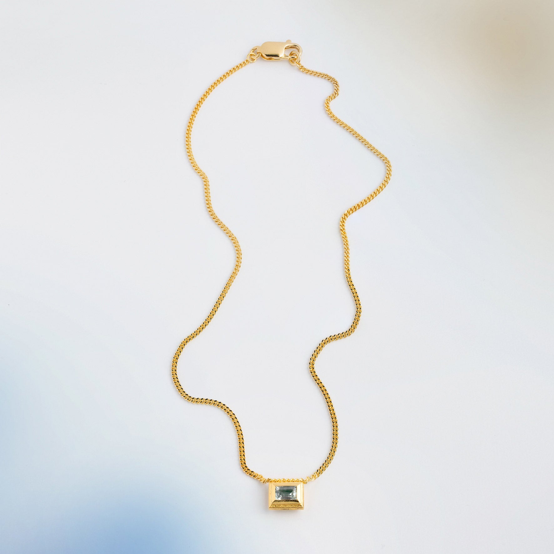 A gold plated silver necklace with a reversible pendant featuring a green Chrysoprase gemstone on one side and blue Topaz on the other designed for everyday wear.