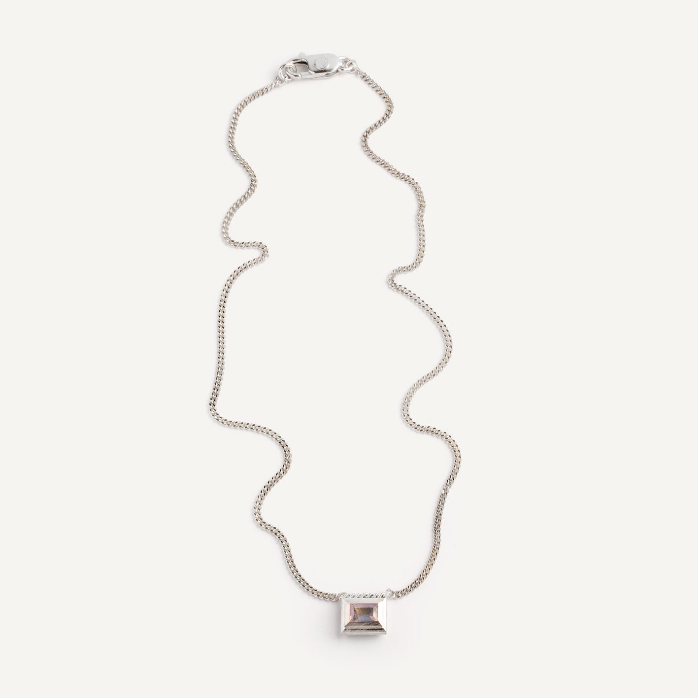 A silver necklace with a reversible pendant featuring a green Peridot gemstone on one side and violet Amethyst on the other designed for everyday wear.