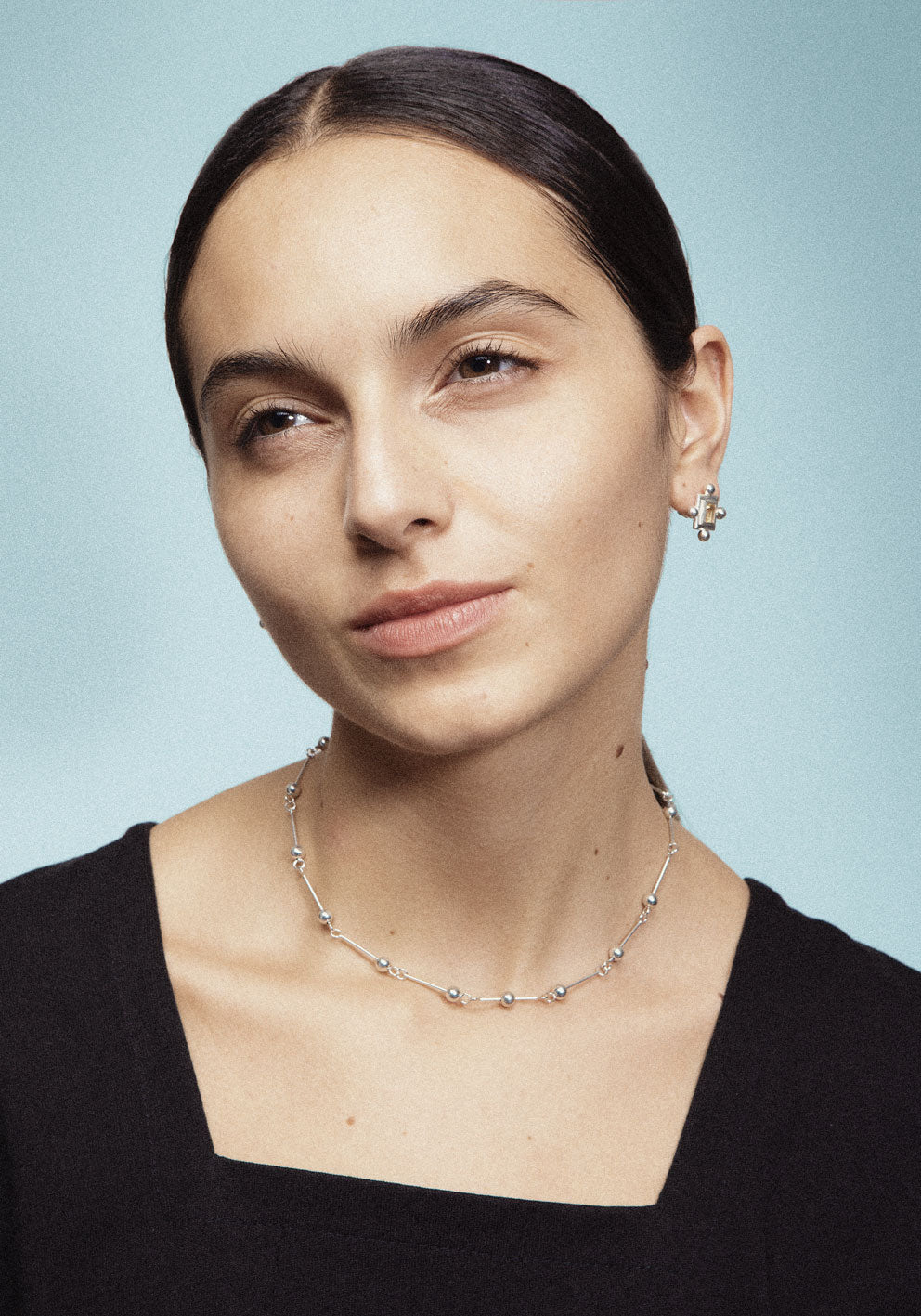 A necklace with small silver spheres strung on silver wire, with a focus on the interplay of light and shadow.