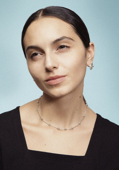 A necklace with small silver spheres strung on silver wire, with a focus on the interplay of light and shadow.