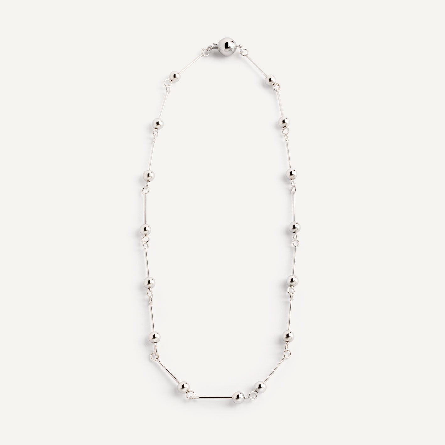 A necklace with small silver spheres strung on silver wire, with a focus on the interplay of light and shadow.