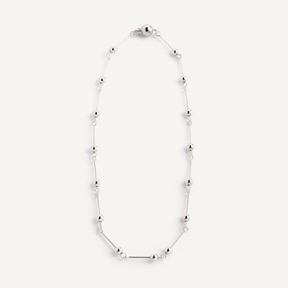 A necklace with small silver spheres strung on silver wire, with a focus on the interplay of light and shadow.